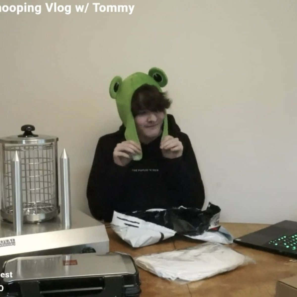 A Man Is Holding A Frog Hat And A Laptop