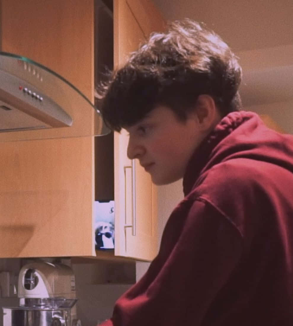 A Young Man In A Red Sweatshirt Is Cooking In A Kitchen