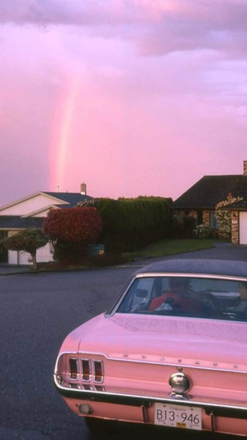 A Pink Mustang Parked In Front Of A House With A Rainbow