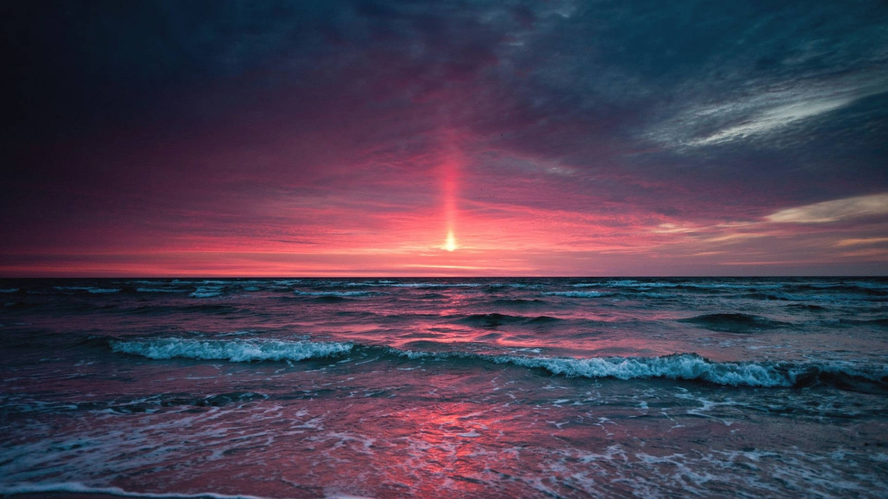 a sunset over the ocean with a red light shining Wallpaper