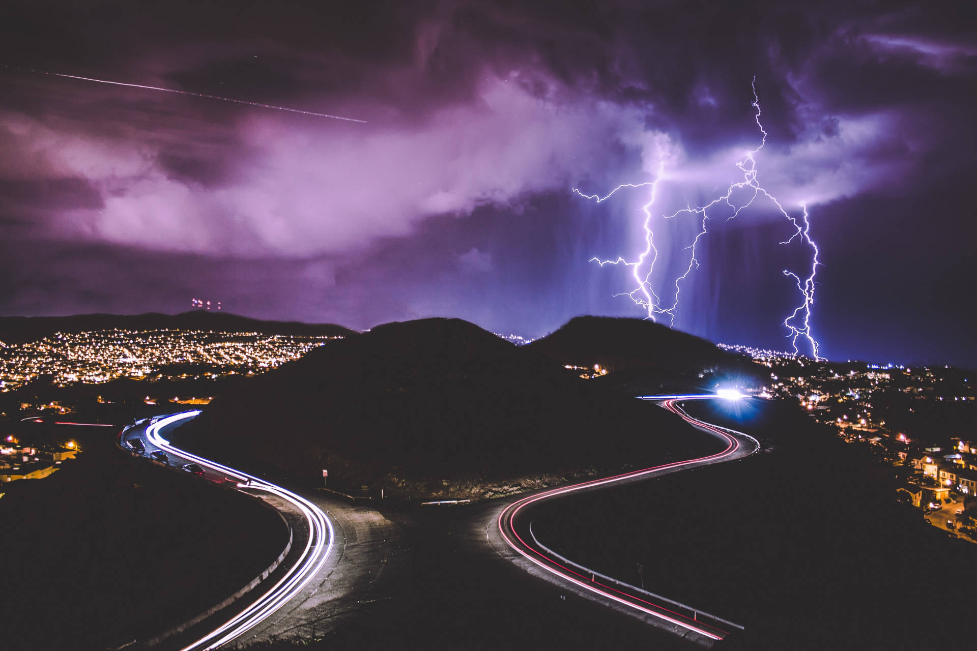 Lightning Over A City With A Road In The Background Wallpaper