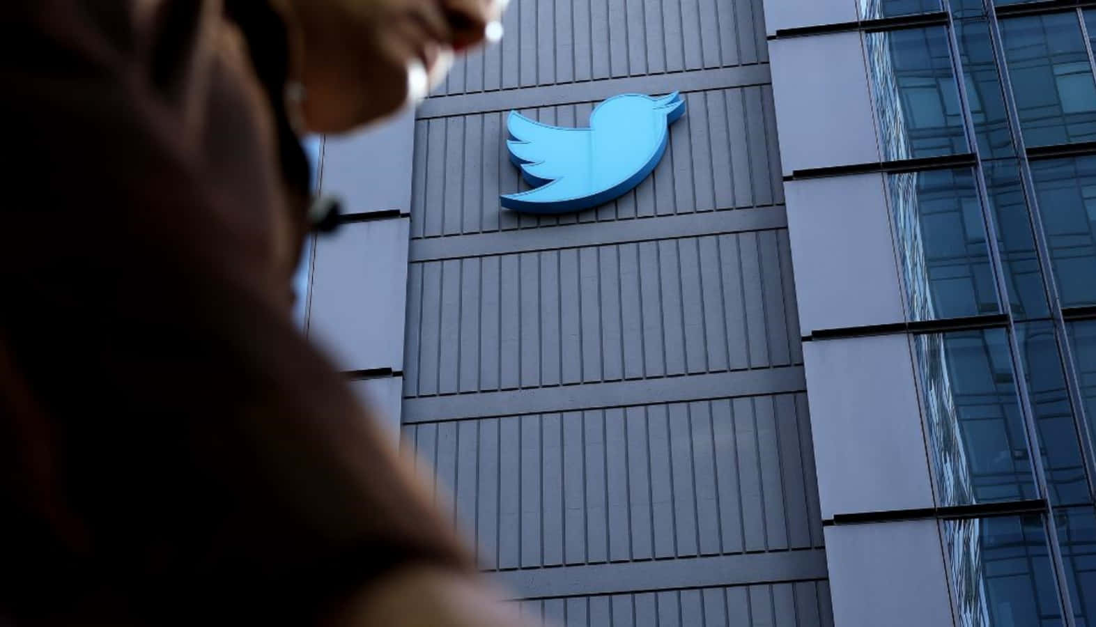A Man Walks Past A Twitter Logo On A Building