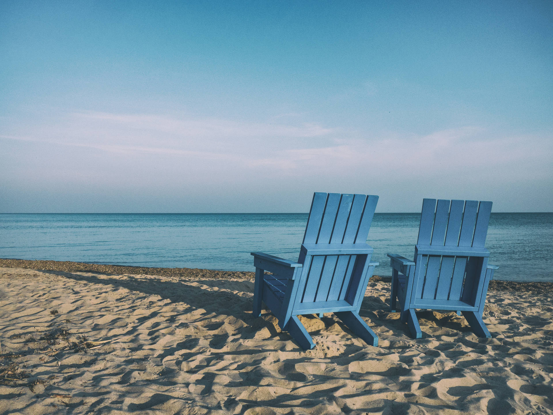 Two blue wooden beach chairs near the sea