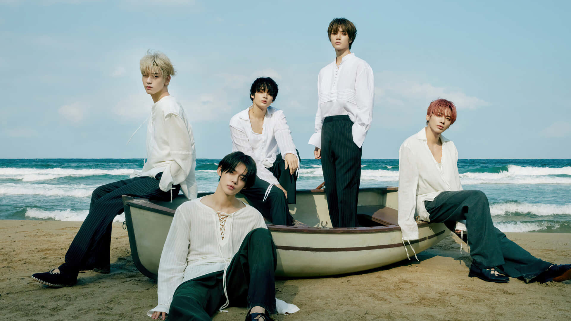 A Group Of Young Men Sitting On A Boat On The Beach Wallpaper