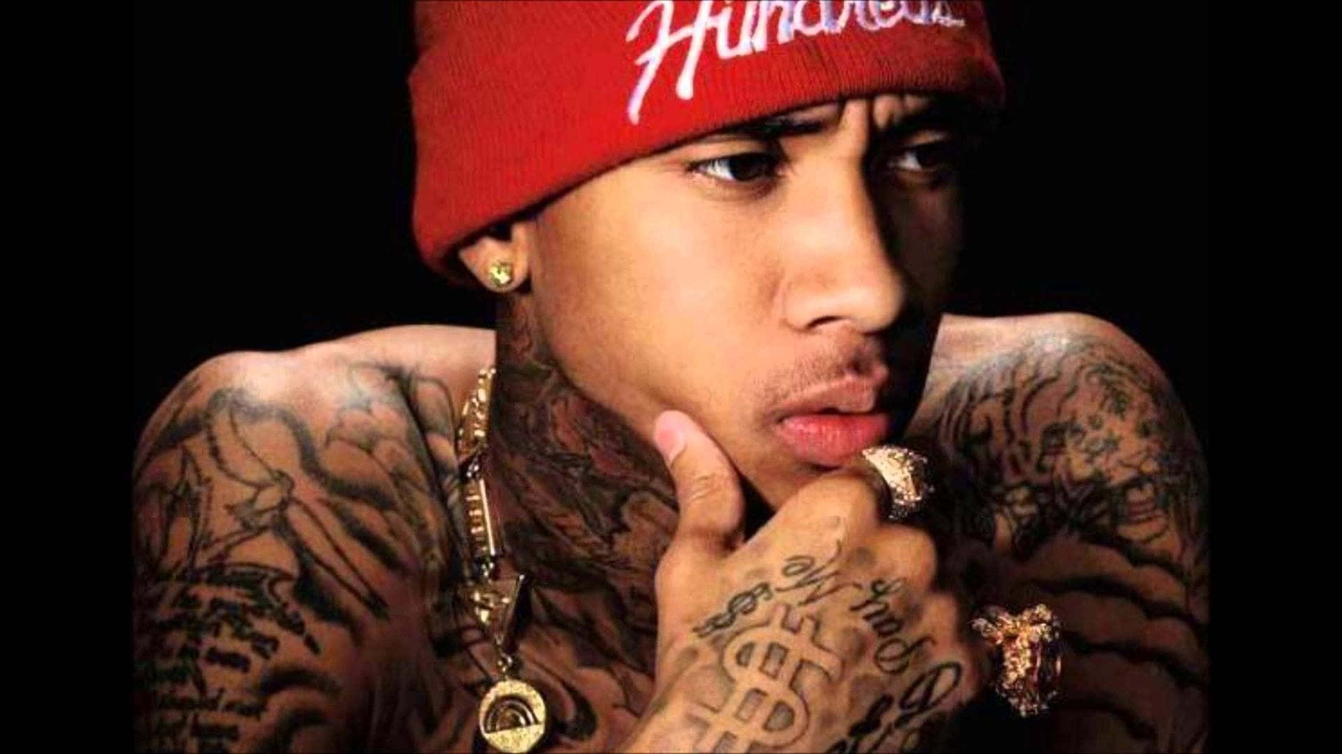 Rapper Tyga | Description: American rapper and entertainer Tyrone William Griffin Jr, or Tyga, poses confidently against a bright red backdrop. | Keywords: Tyga, rap, hip hop, entertainer, musician, Tyrone William Griffin Jr. Wallpaper