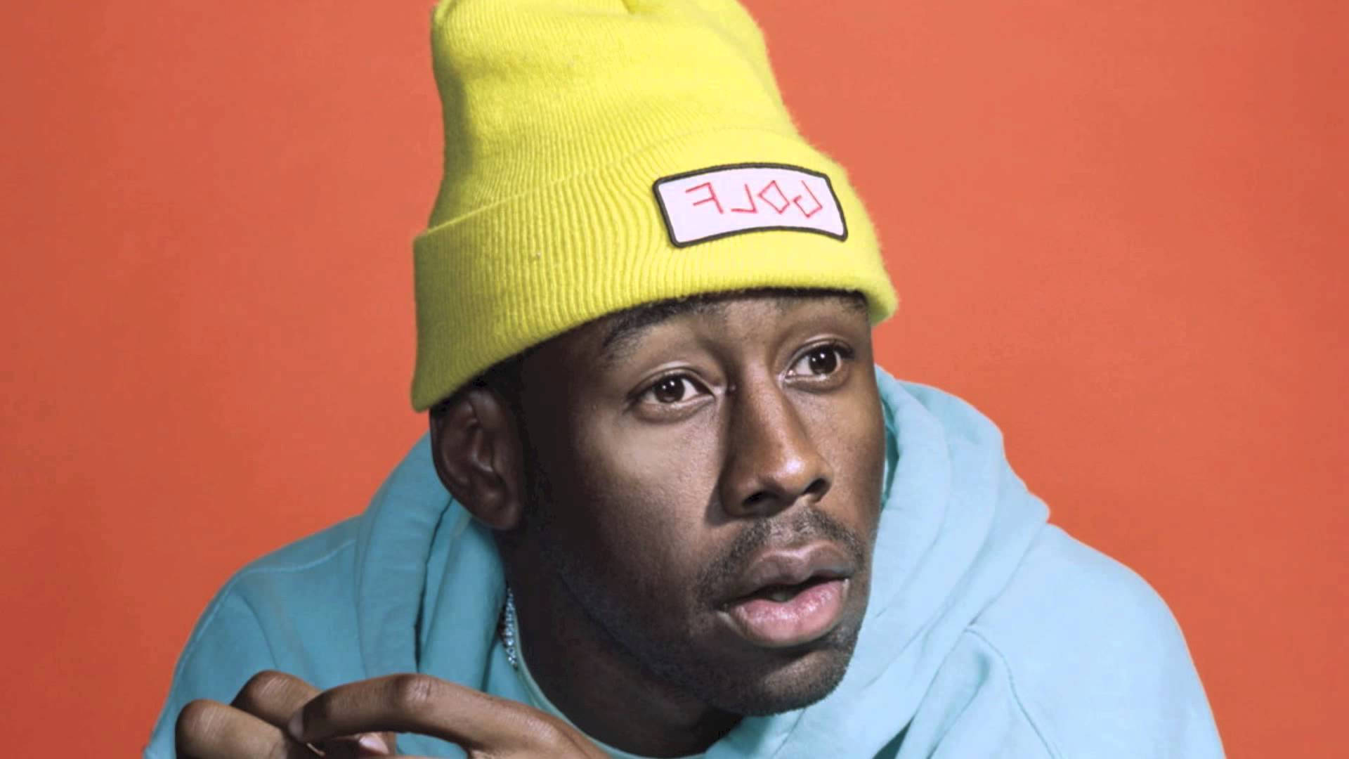 Tyler The Creator looking confident and relaxed in an orange background Wallpaper