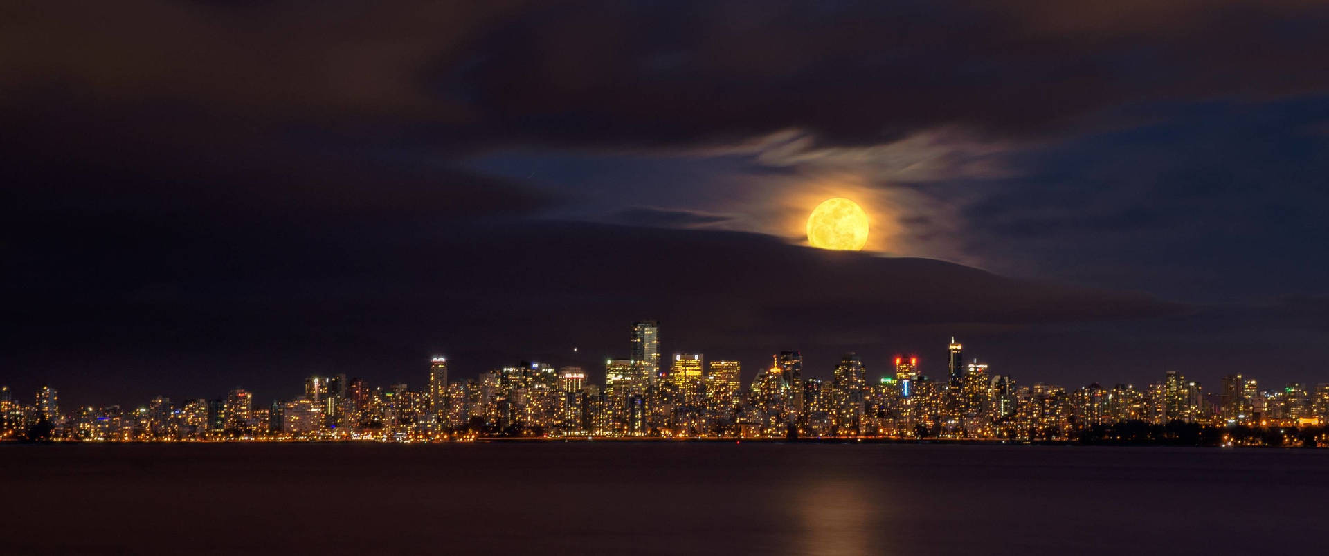 Ultrawide view of city from afar with yellow moon on a dark gloomy sky.