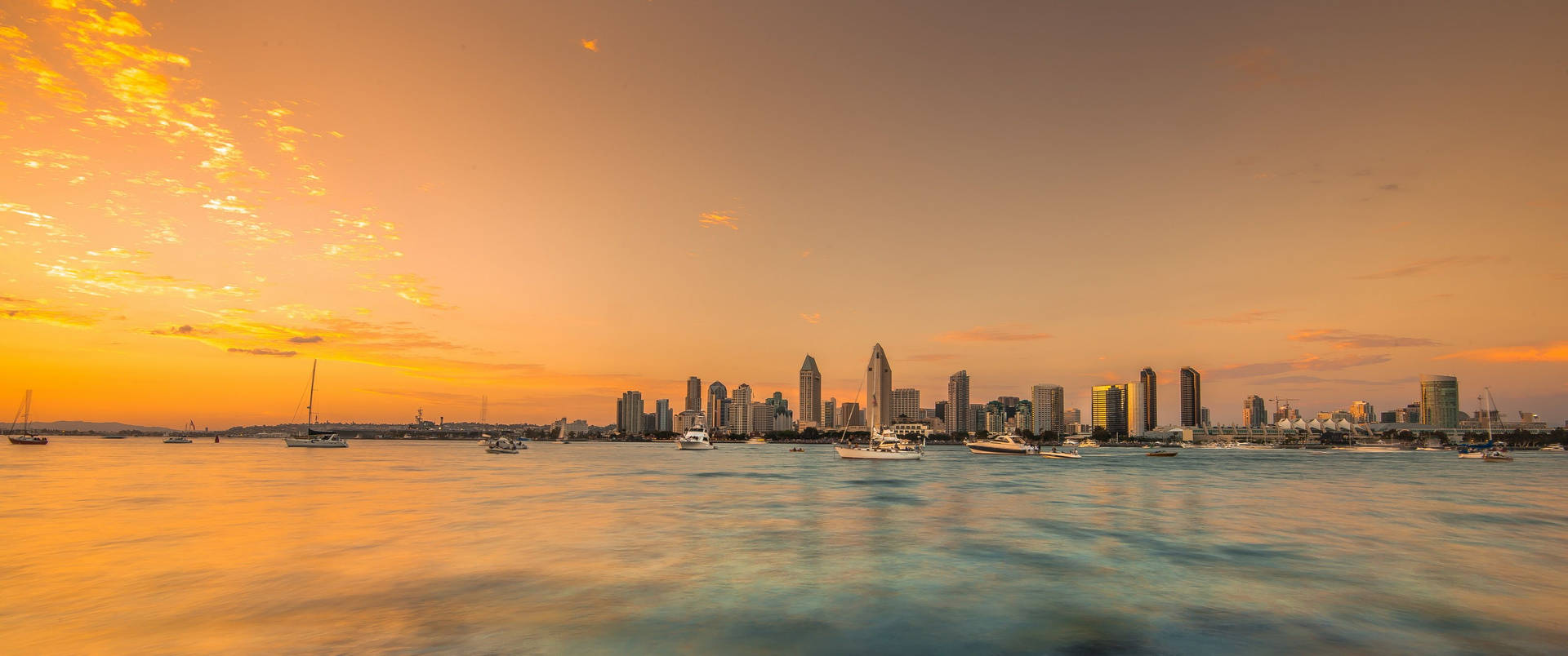 Ultrawide sunset on sea showing tall buildings from afar.