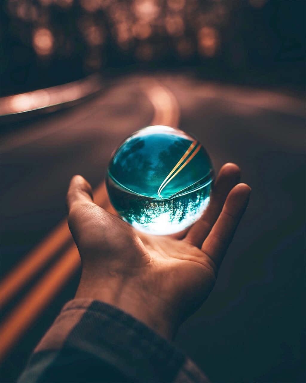 A Person Holding A Glass Ball On A Road
