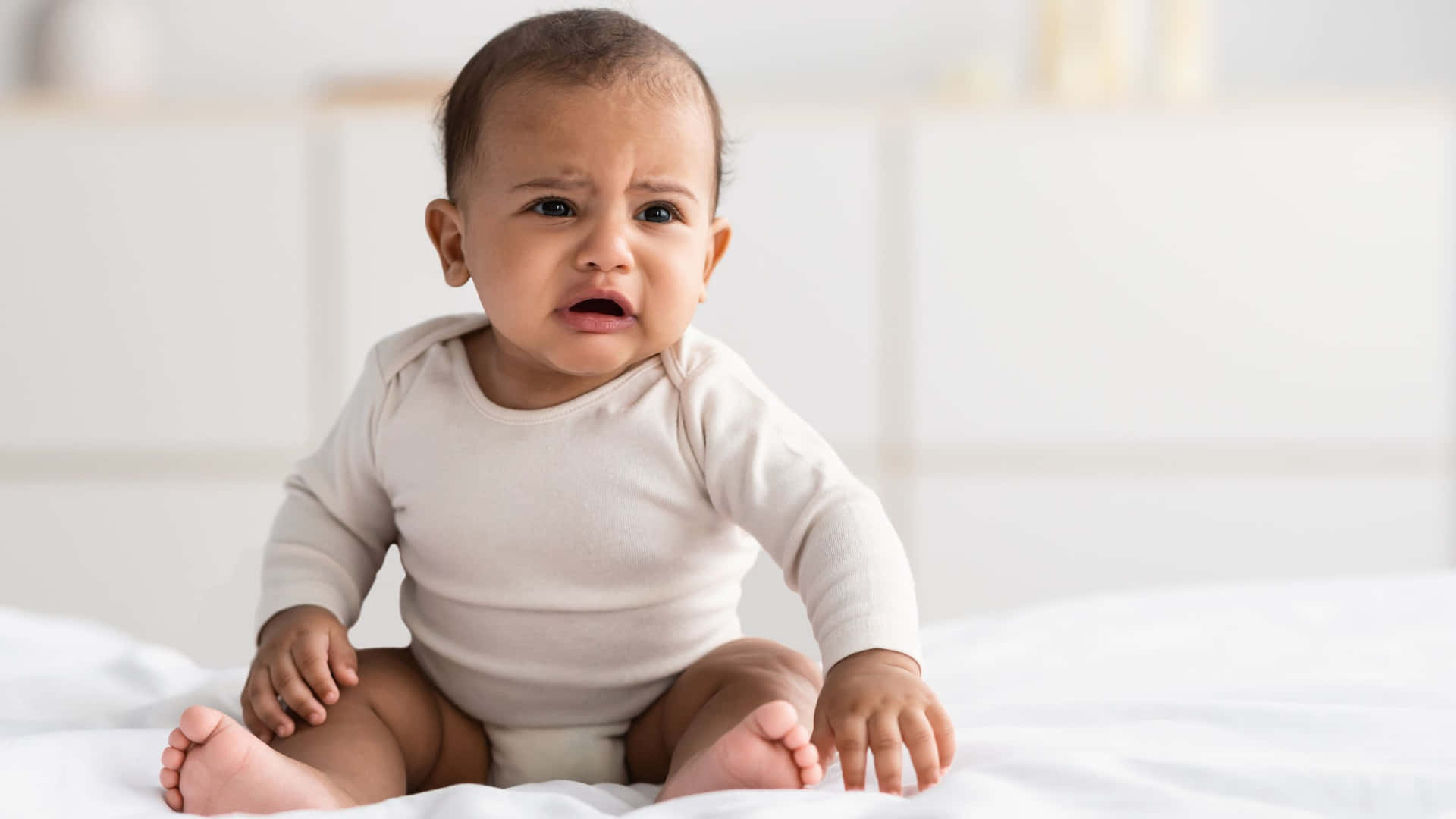 Upset Baby Sitting On Bed Wallpaper