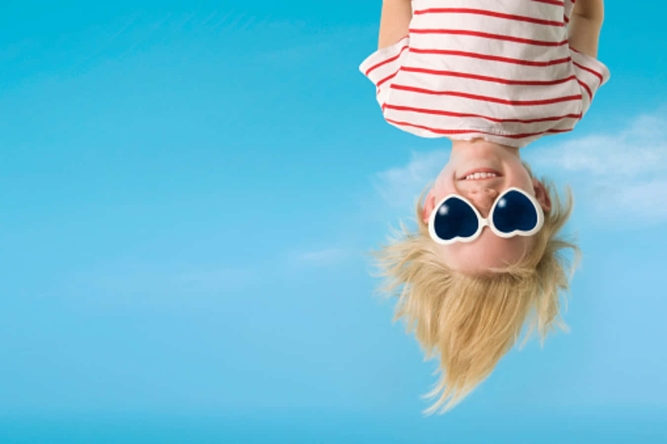En pige er op ned i luften med solbriller og hat.