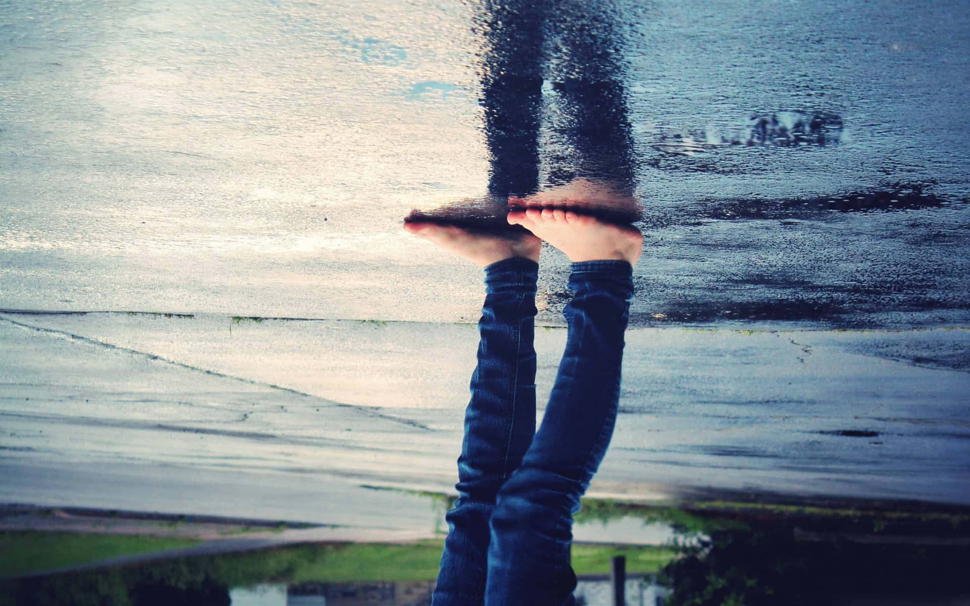 En person stående på et vådt fortov ved en spejlvandbassin.