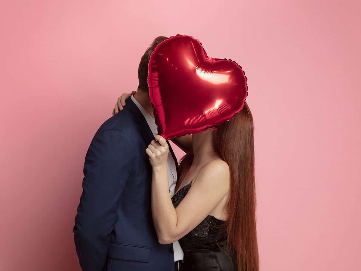 A Man And Woman Kissing With A Heart Shaped Balloon