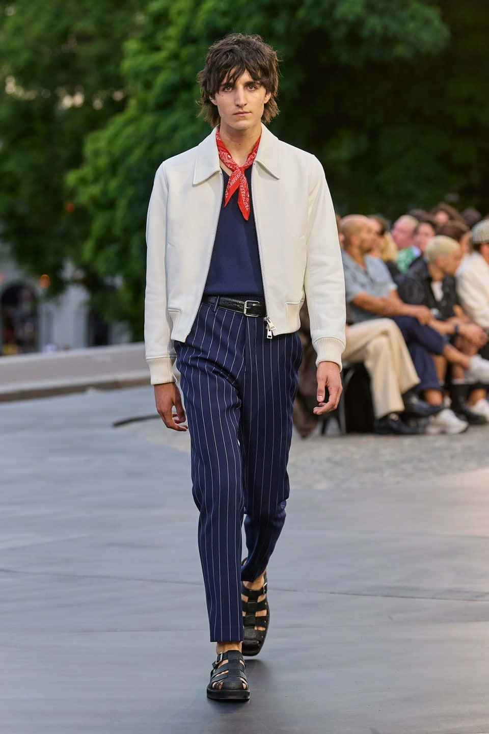 A Man In A White Jacket And Striped Pants Walks Down The Runway