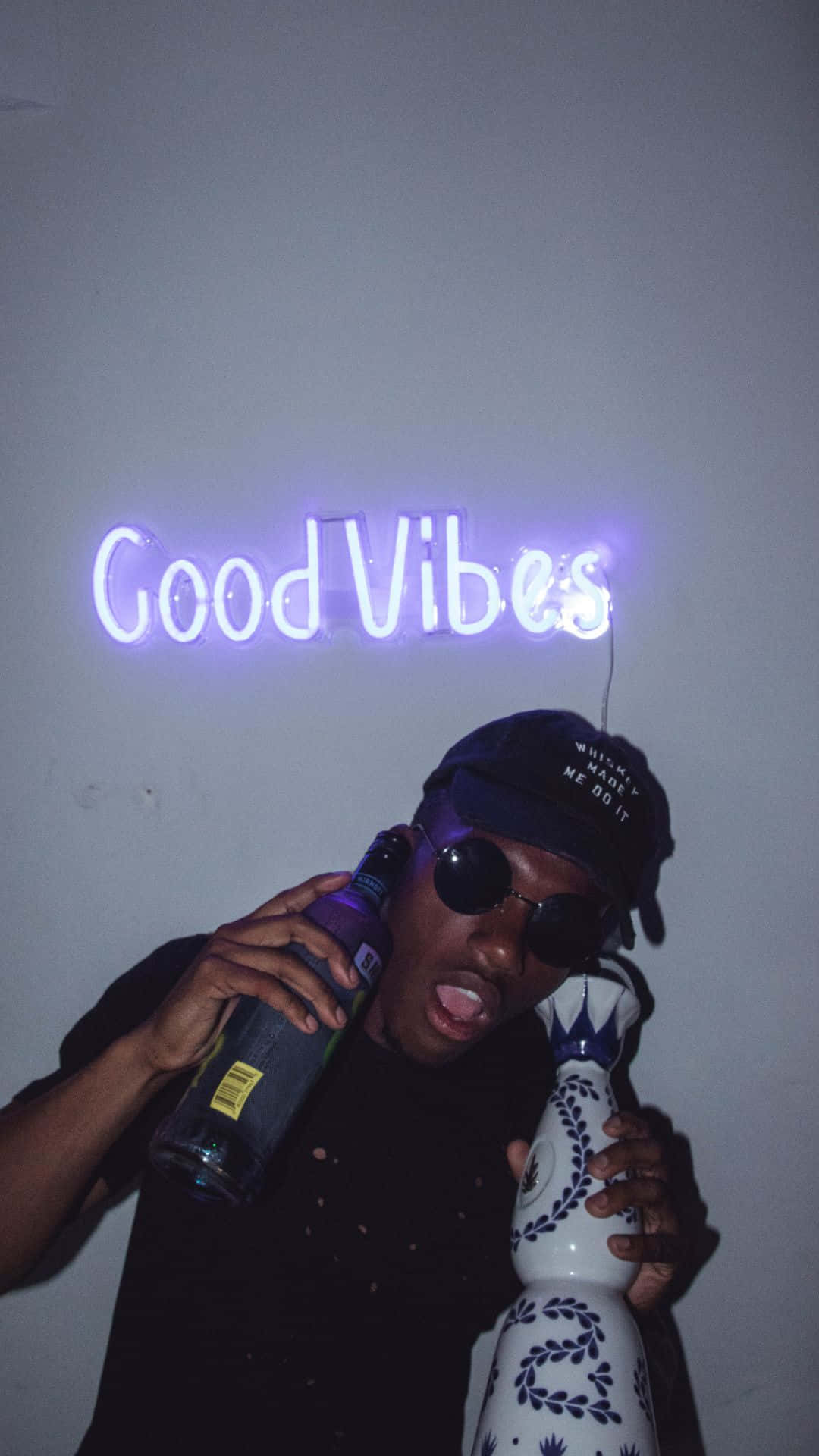 A Man Holding A Bottle Of Liquor And A Neon Sign That Says Good Vibes Wallpaper