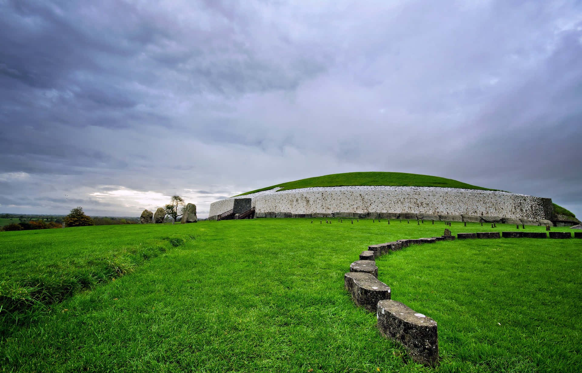 Vibrant Newgrange Passage Tomb With Stormy Cloud Wallpaper