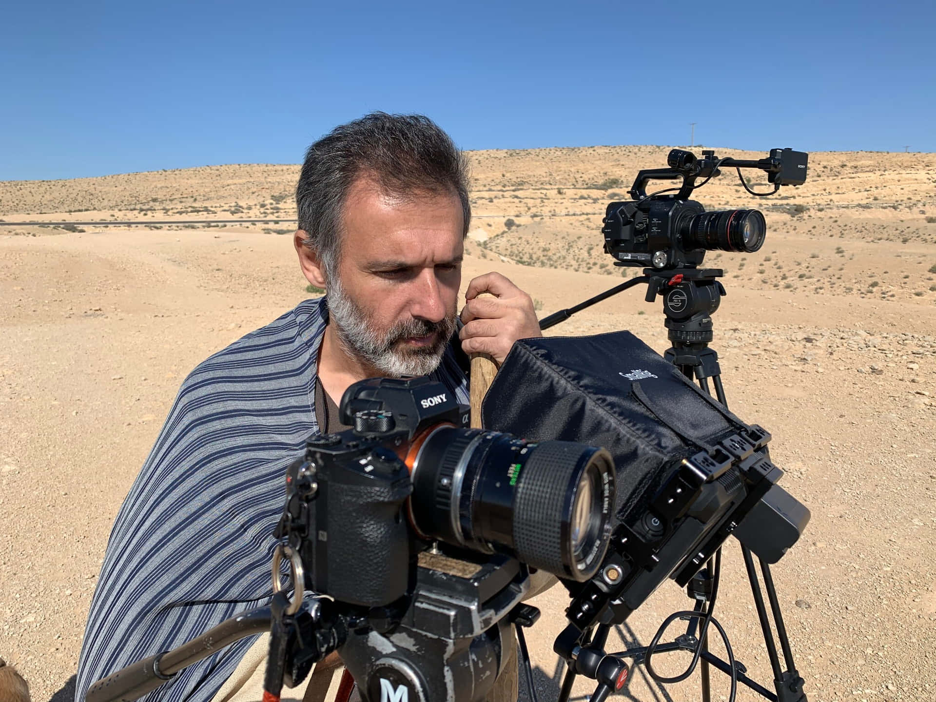A Man In A Blanket Is Holding A Camera In The Desert