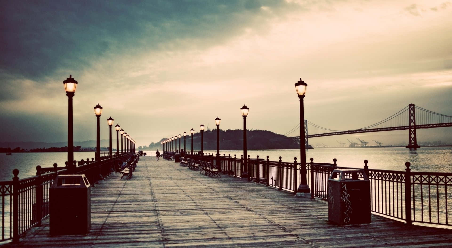 A Pier With Benches And A Bridge In The Background Wallpaper