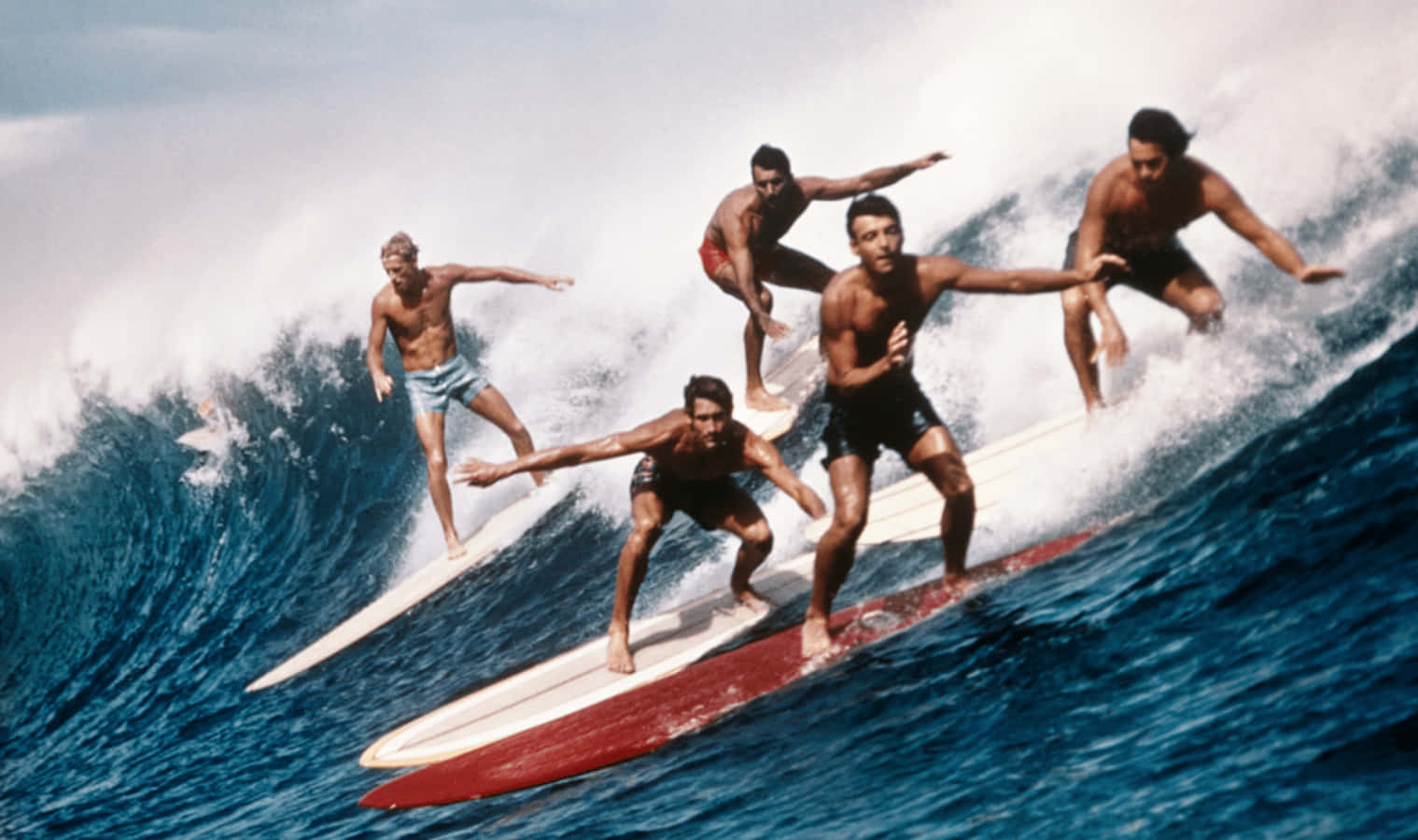 Ungrupo De Surfistas Montando Una Ola En Tablas De Surf. Fondo de pantalla