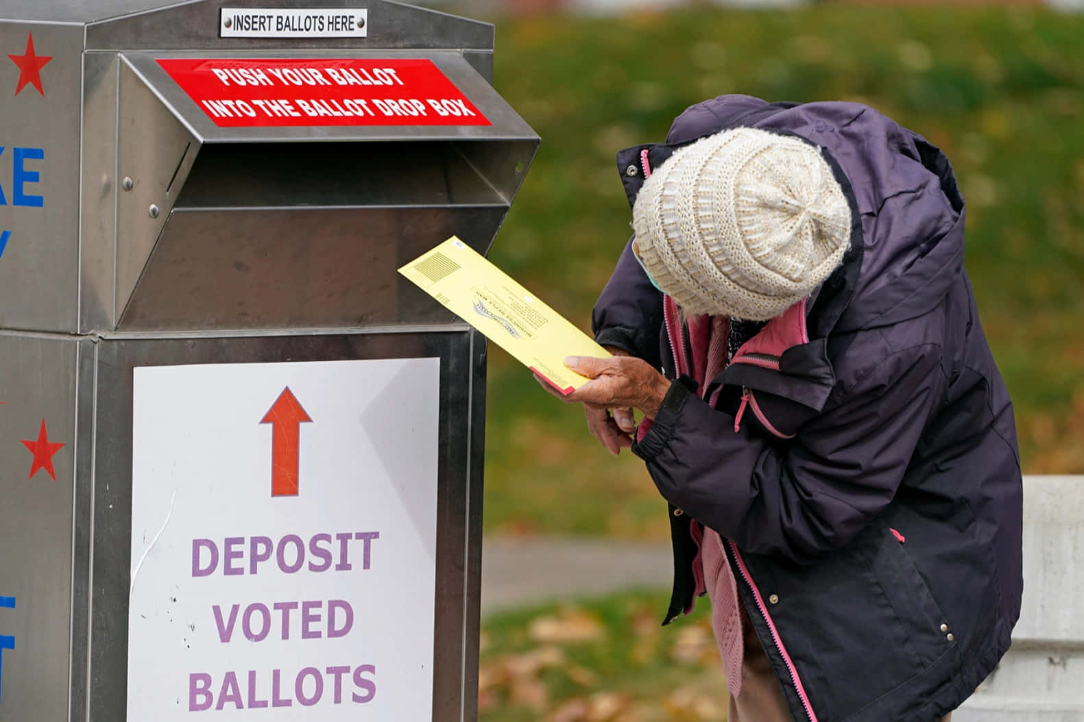 A Woman Is Putting Her Ballot In A Mailbox