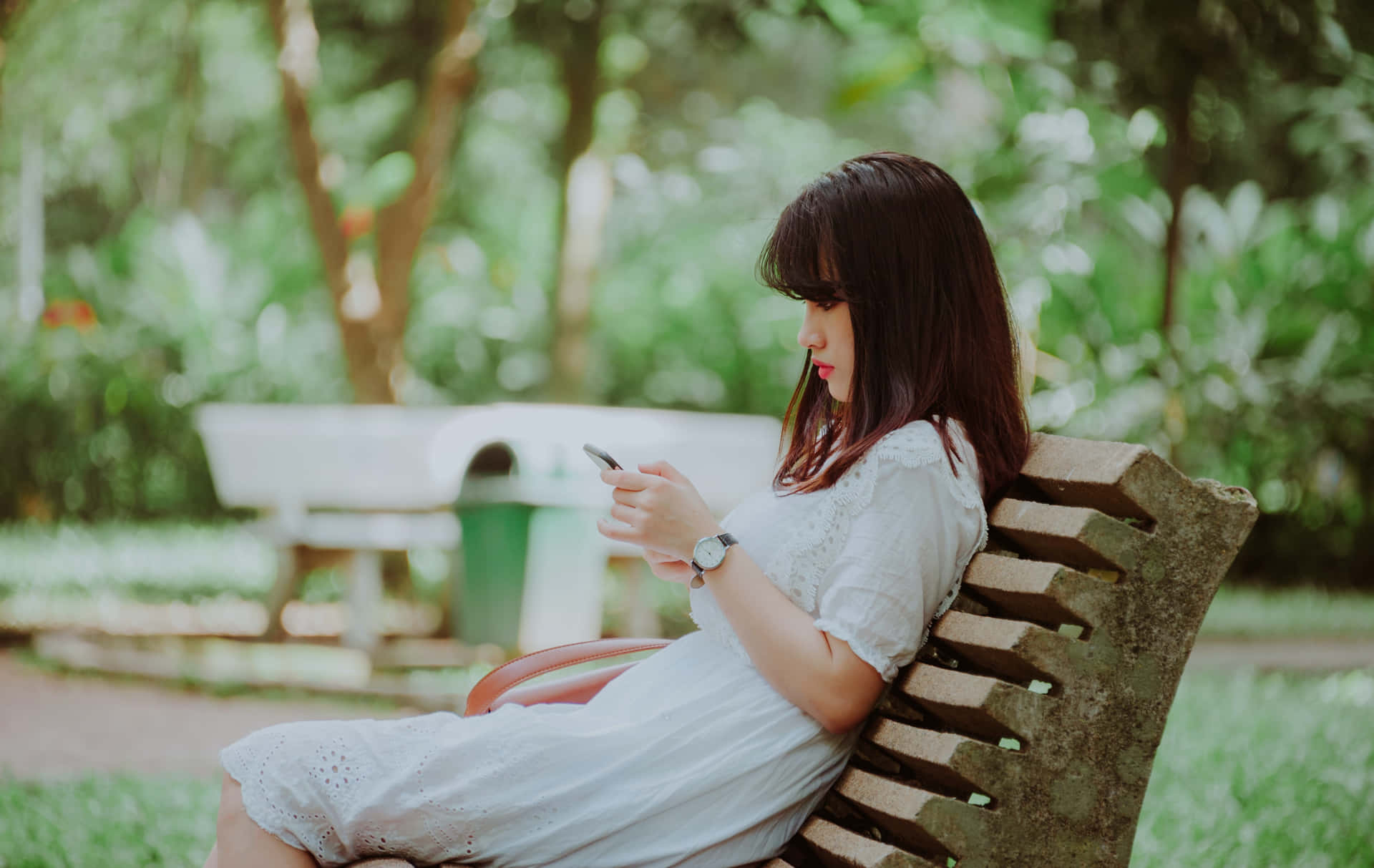 A Woman Sitting On A Bench Looking At Her Phone