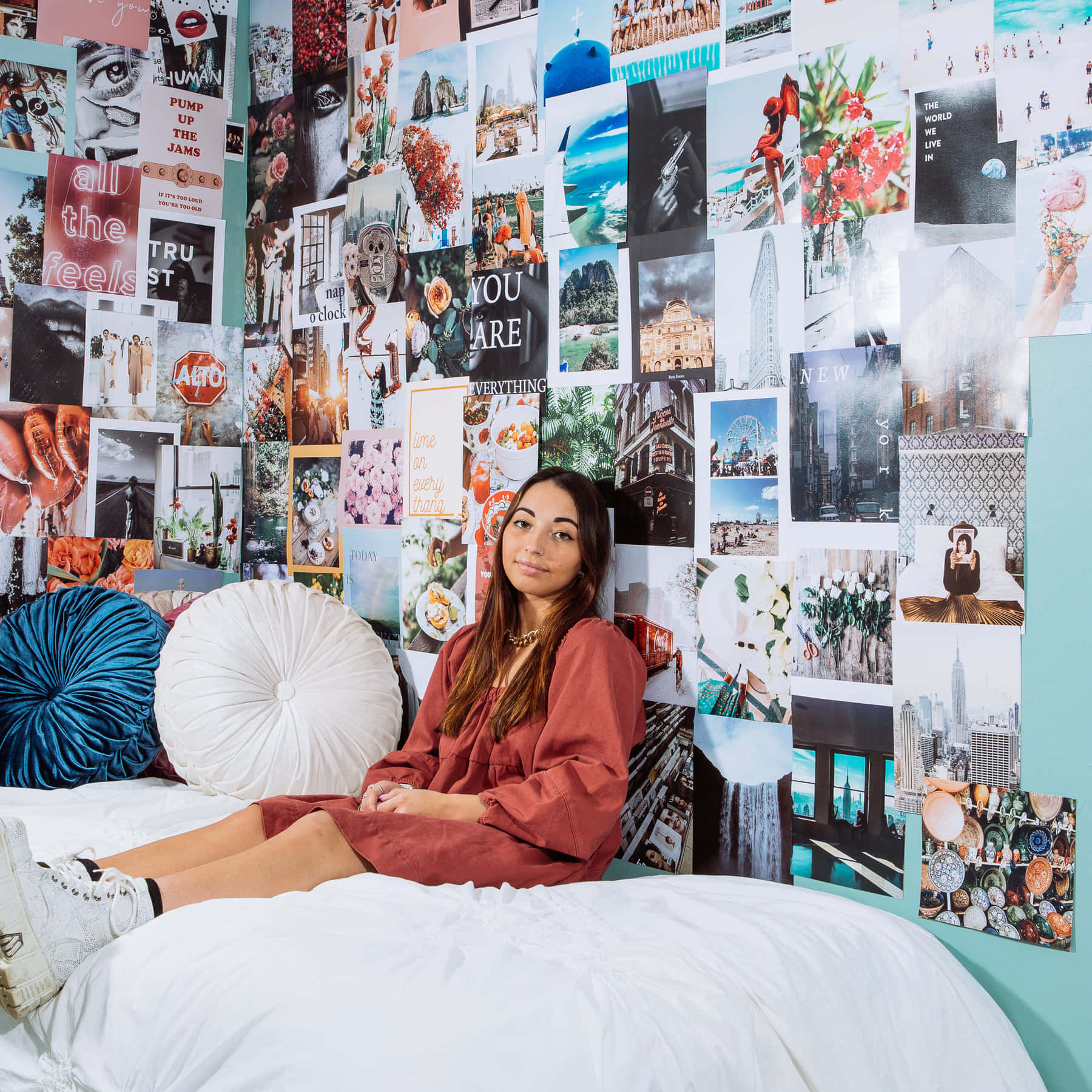 A Girl Sitting On A Bed With A Lot Of Pictures On The Wall