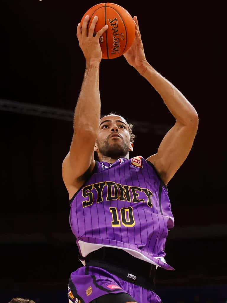 Xavier Cooks Wallpaper — A basketball player in a purple Sydney Kings jersey shoots a Spalding ball with intense focus under arena lights.