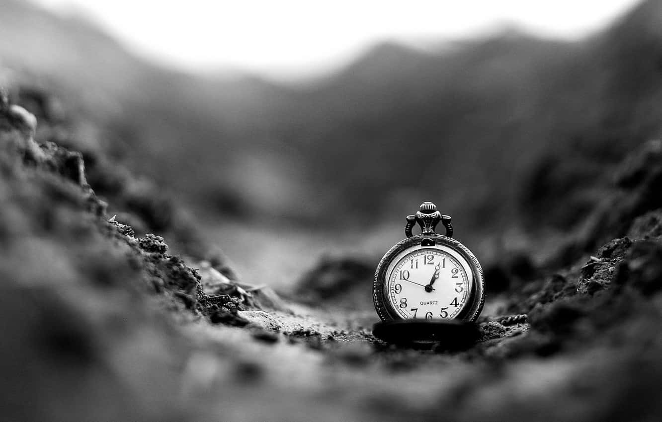 A Black And White Photograph Of A Clock In The Dirt