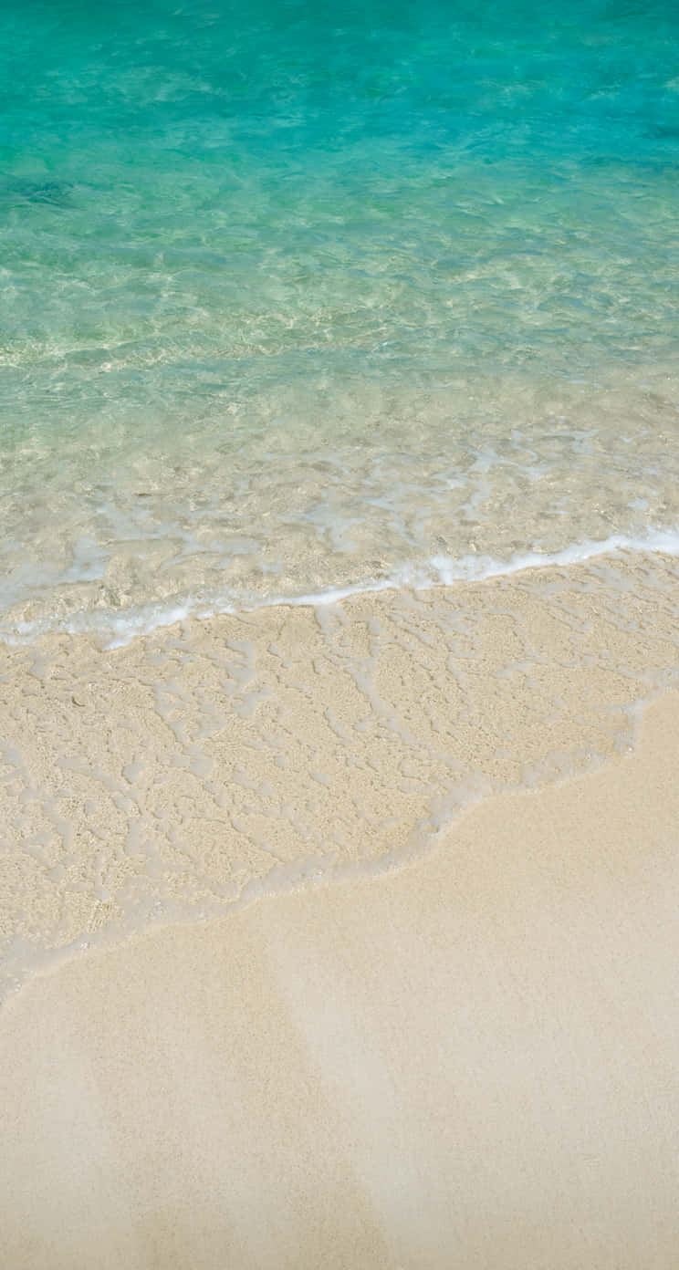 Unhombre Está Caminando En Una Playa Arenosa Con Agua. Fondo de pantalla