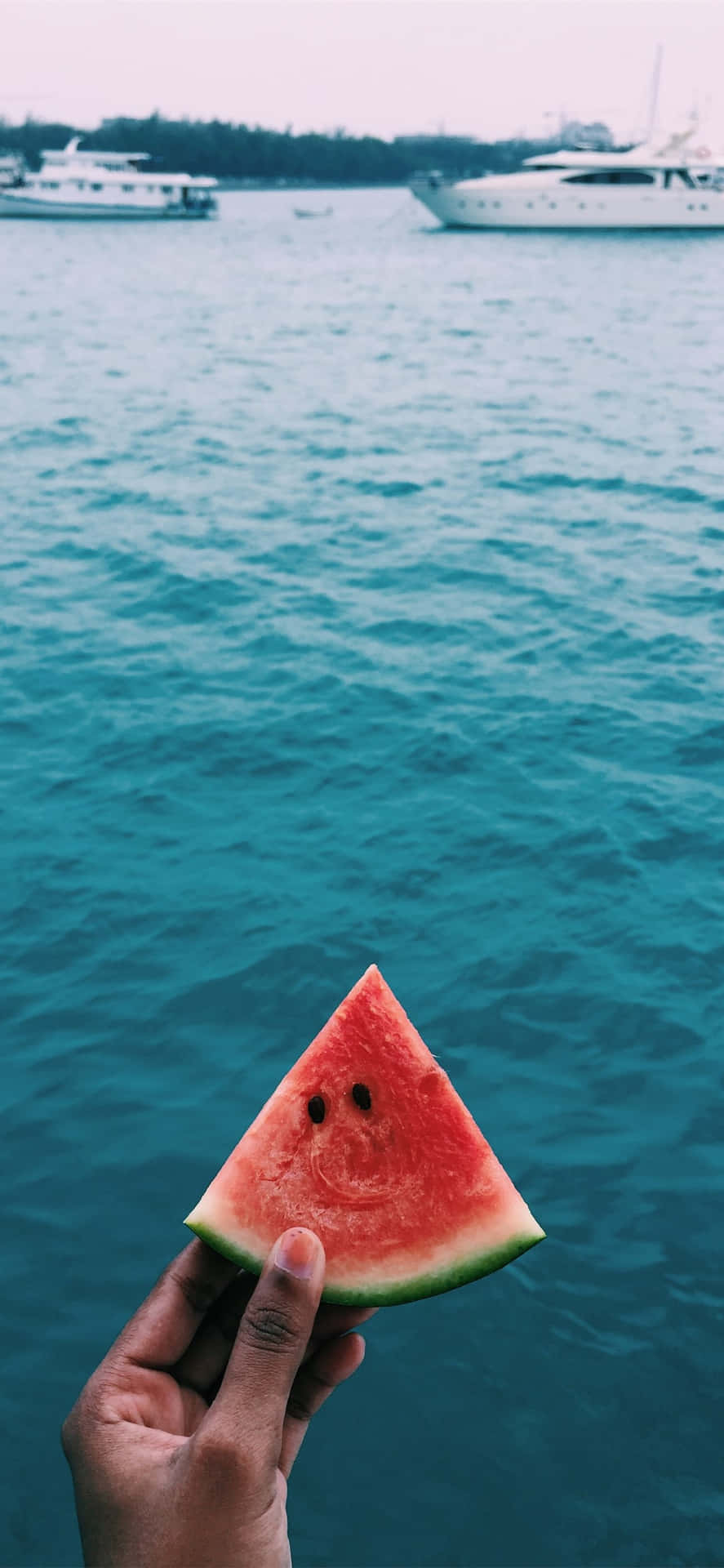 En person holder et skive vandmelon foran et båd Wallpaper