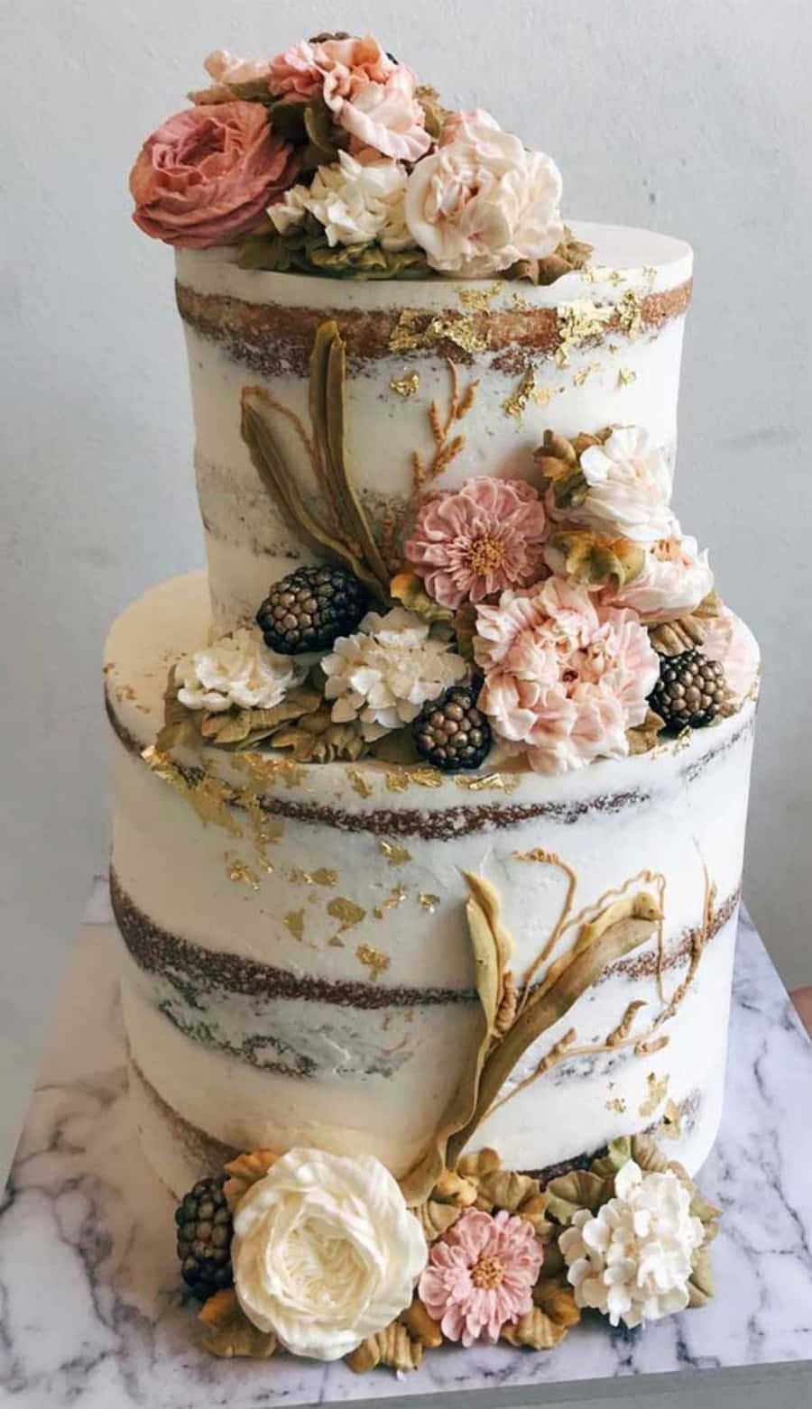 A Three Tier Cake With Flowers And Gold Decorations