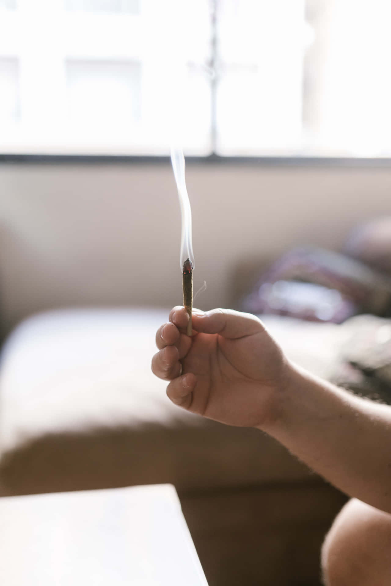 A hand holds a freshly lit weed blunt, smoke slowly curling around it. Wallpaper