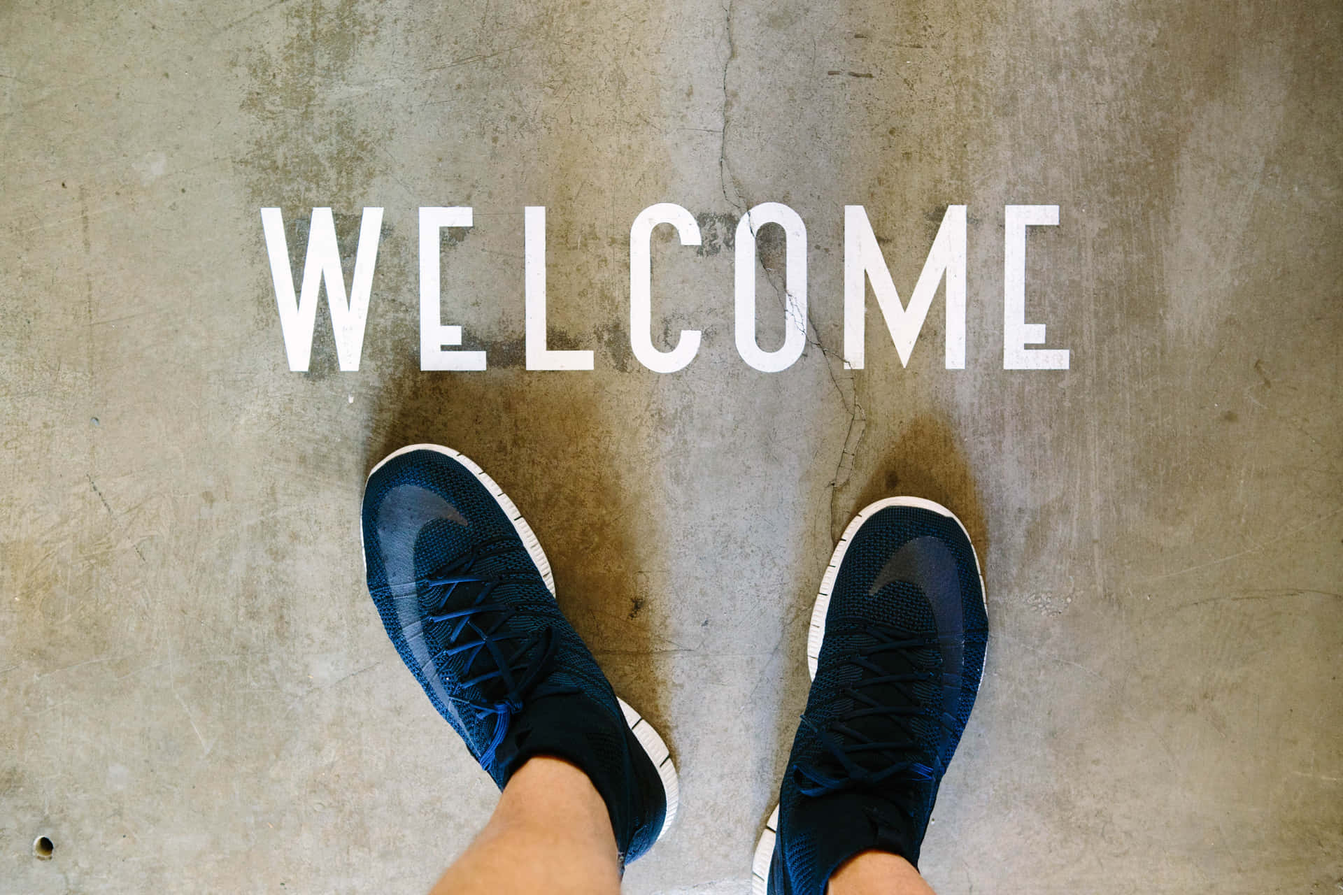 A Person's Feet Standing On A Concrete Floor With The Word Welcome