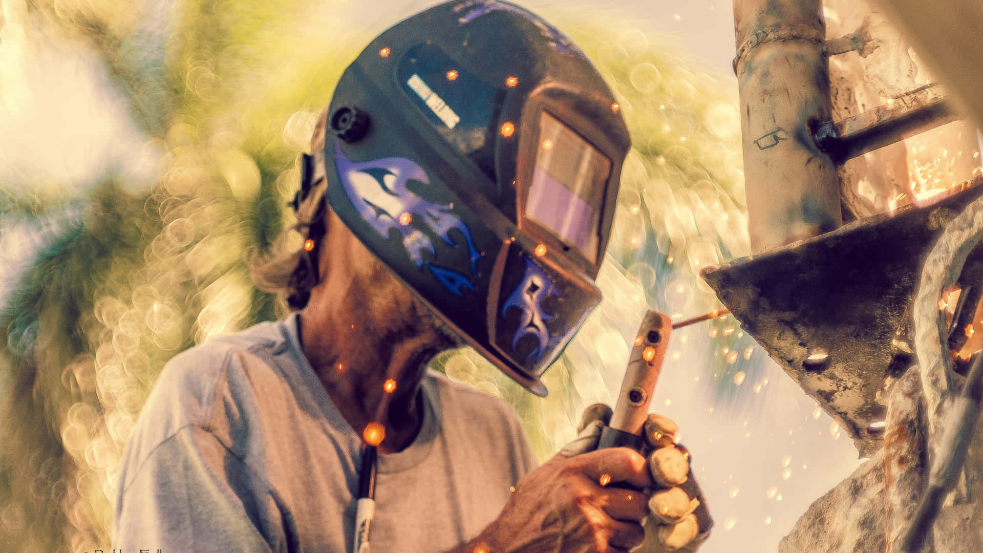A Man Welding With A Helmet On A Piece Of Metal Wallpaper