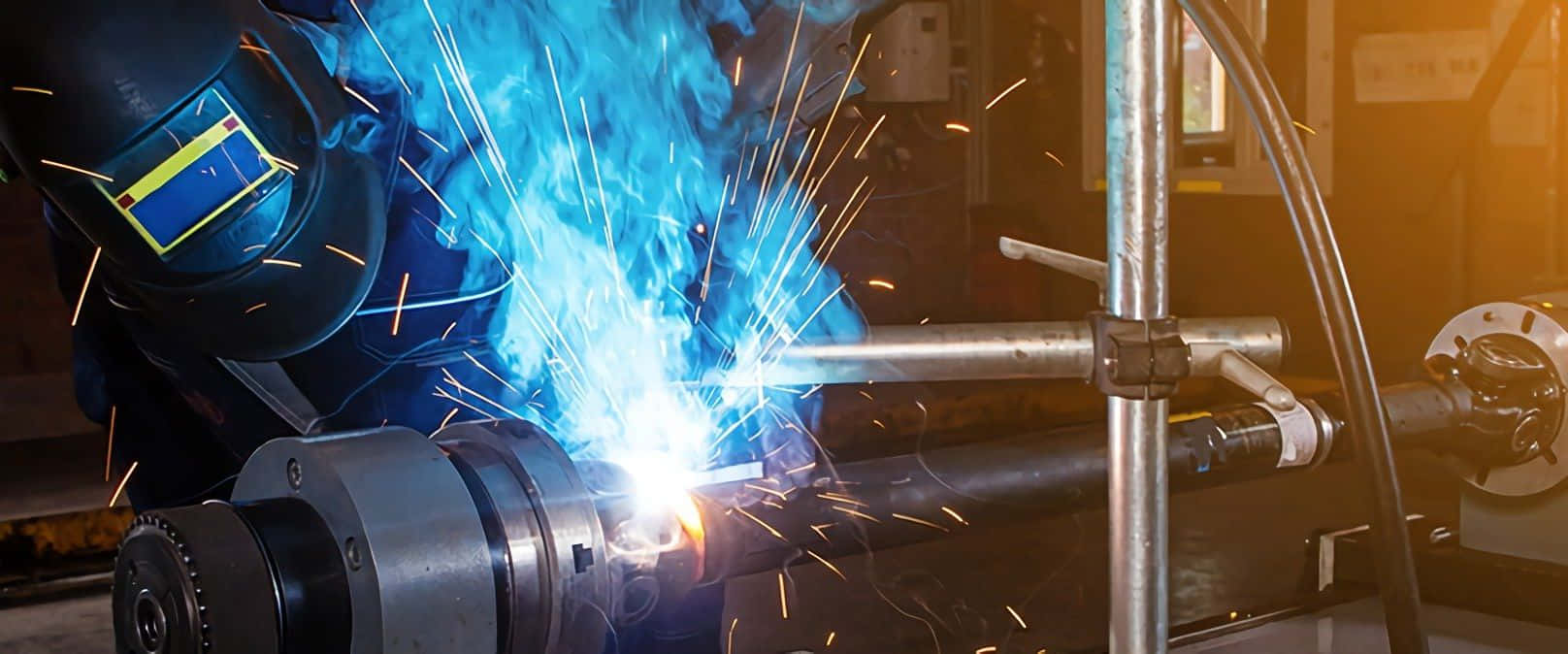 A Worker Is Welding A Metal Pipe With Blue Flames Wallpaper