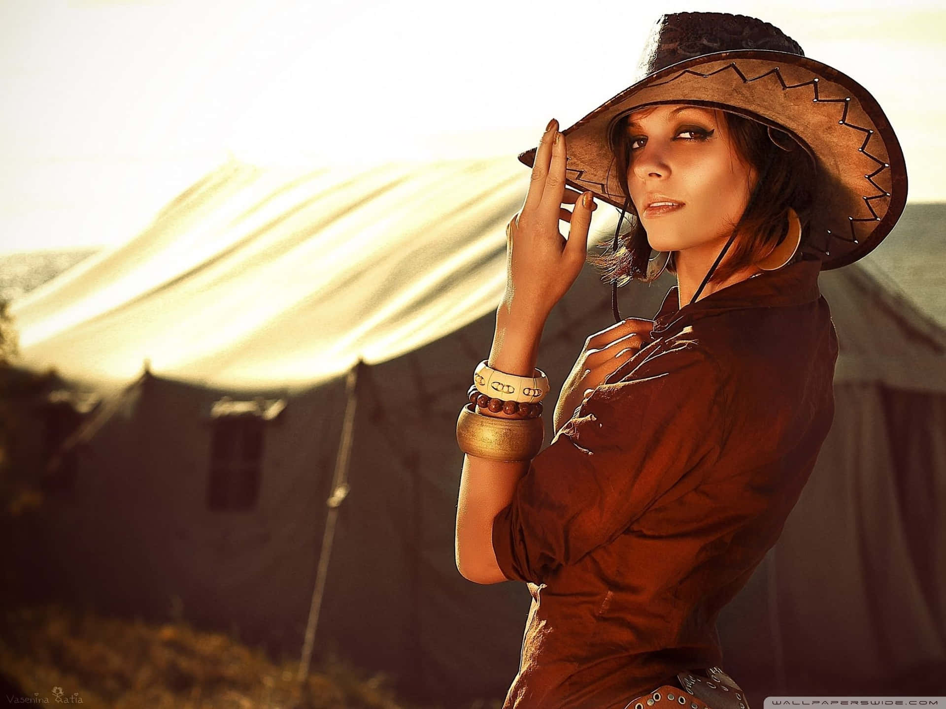 En kvinde iført en cowboyhat, stående foran et vindmølle. Wallpaper
