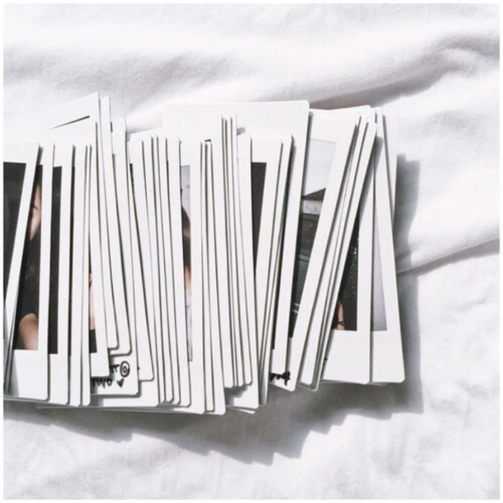 A Pile Of Polaroid Photos On A White Bed