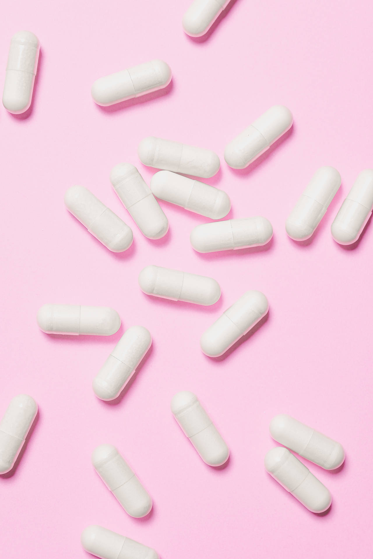 White Capsules On Pink Background Wallpaper