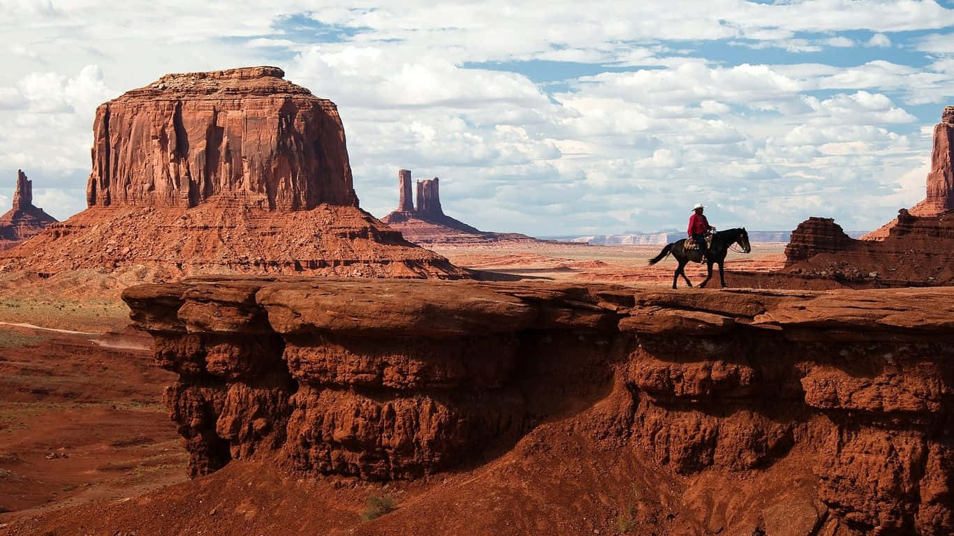 En mand rider en hest på en klippe i Monument Valley Wallpaper
