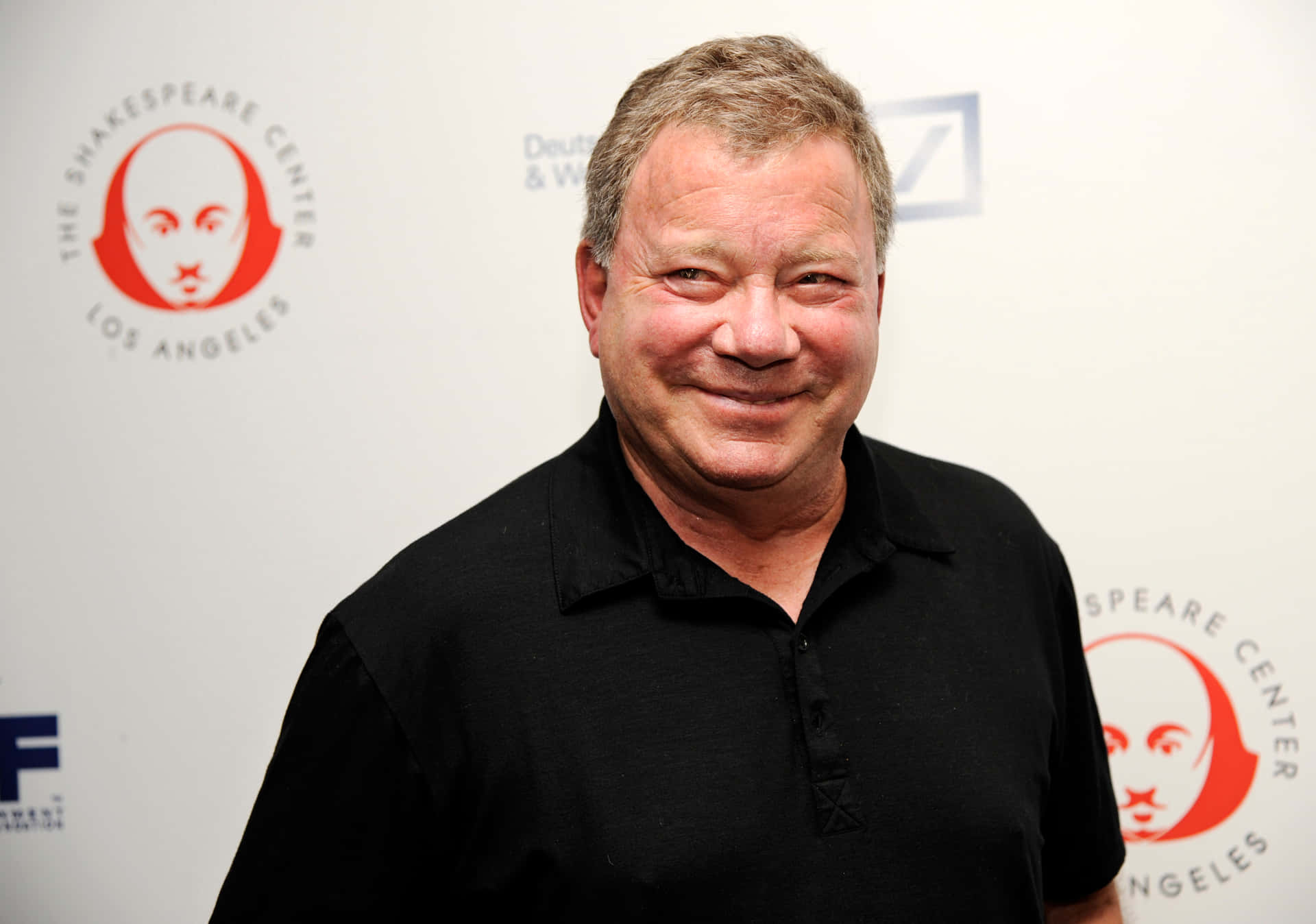 Williamshatner Sonriendo En Un Traje Negro Con Una Camisa Azul. Fondo de pantalla