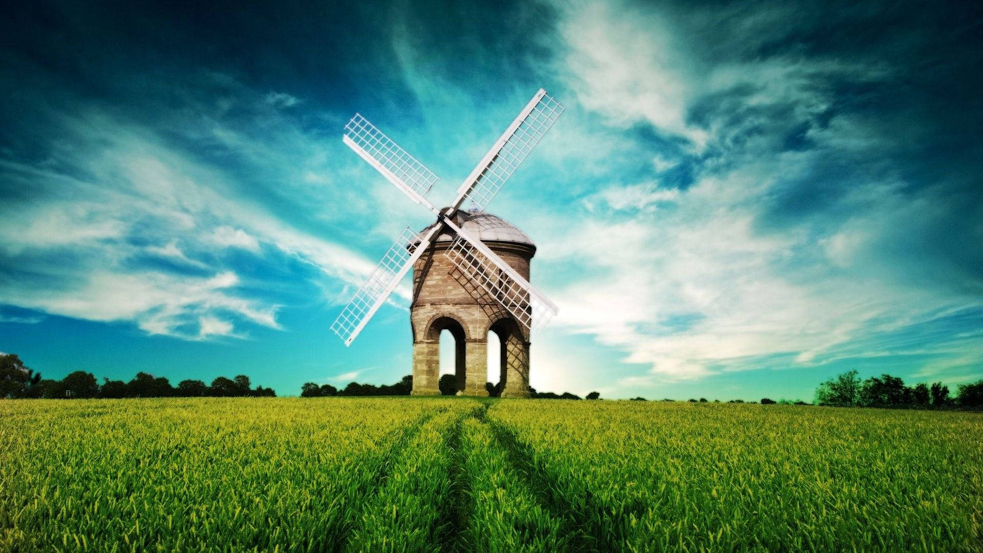 An aerial view of a windmill against a grass-filled landscape Wallpaper