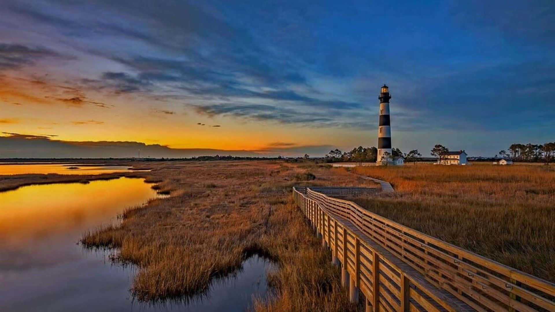 A Lighthouse Is Seen At Sunset Near A Marsh Wallpaper