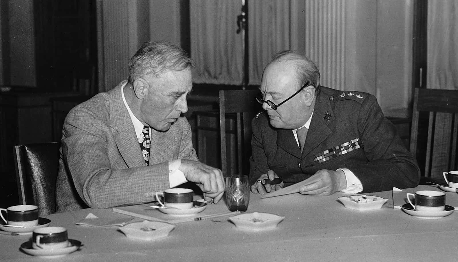 Two Men Sitting At A Table With Cups Of Tea