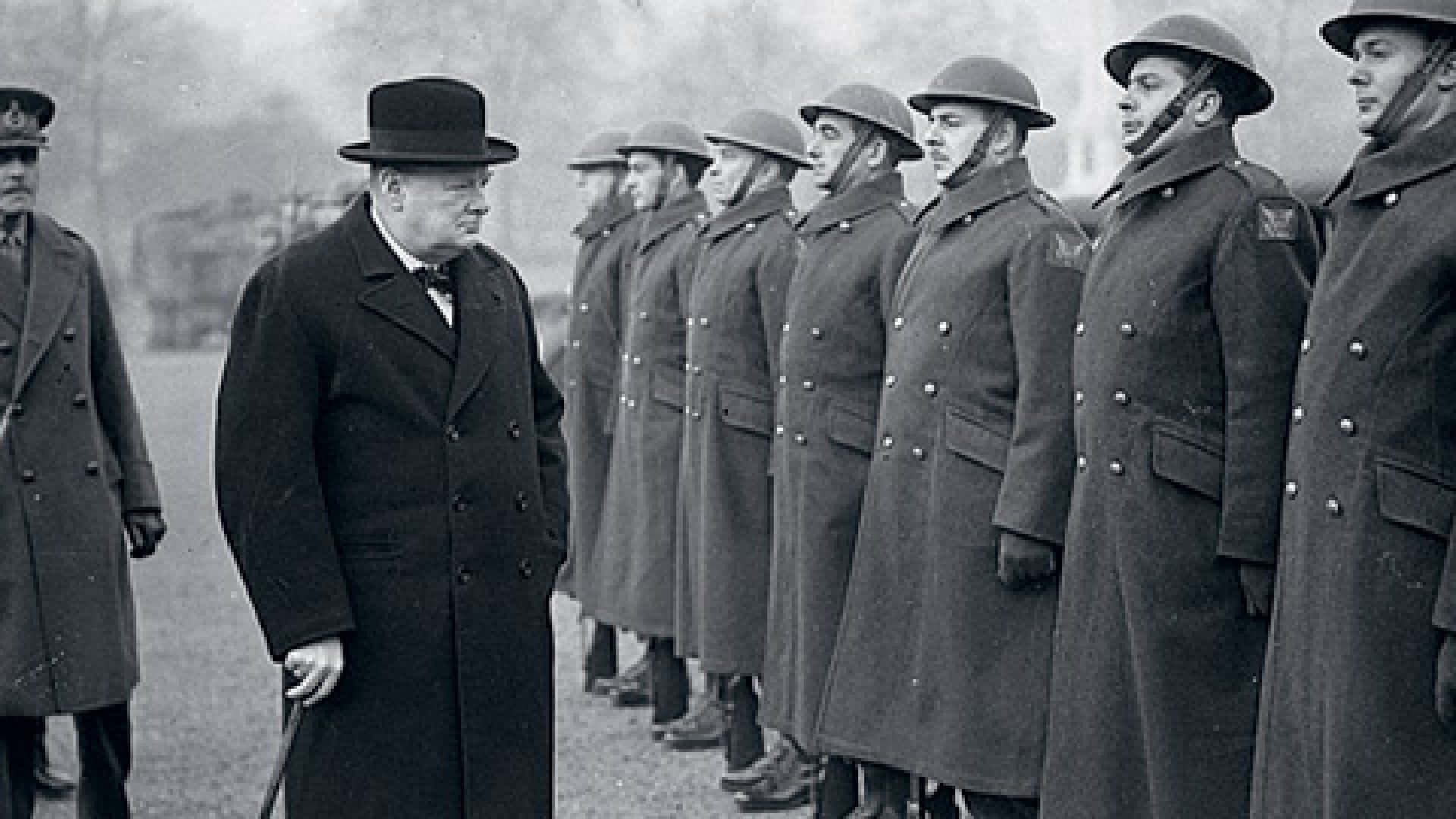A Man In A Hat And Coat Standing In Front Of A Group Of Men