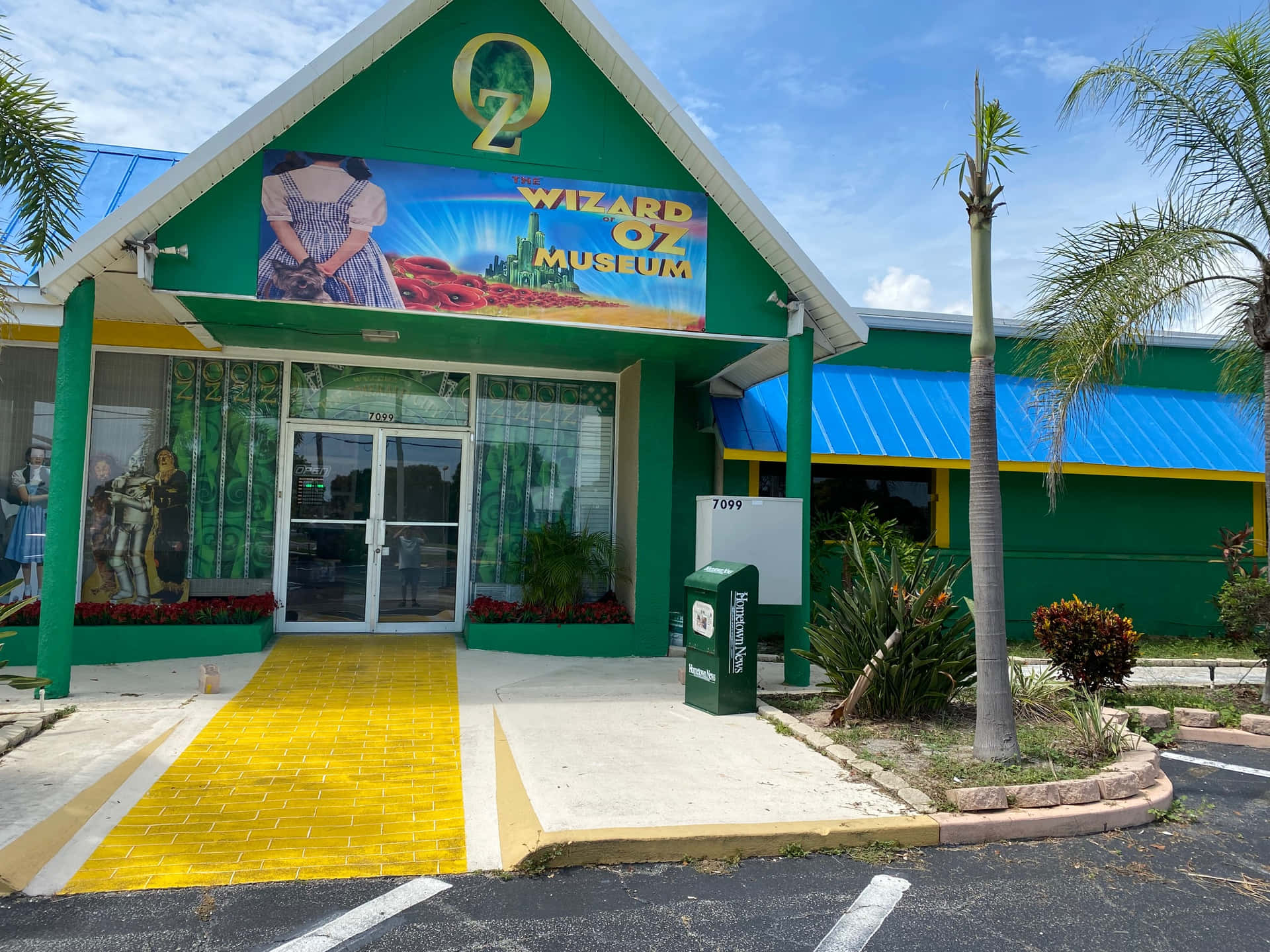 A Yellow And Green Building With Palm Trees And A Sign
