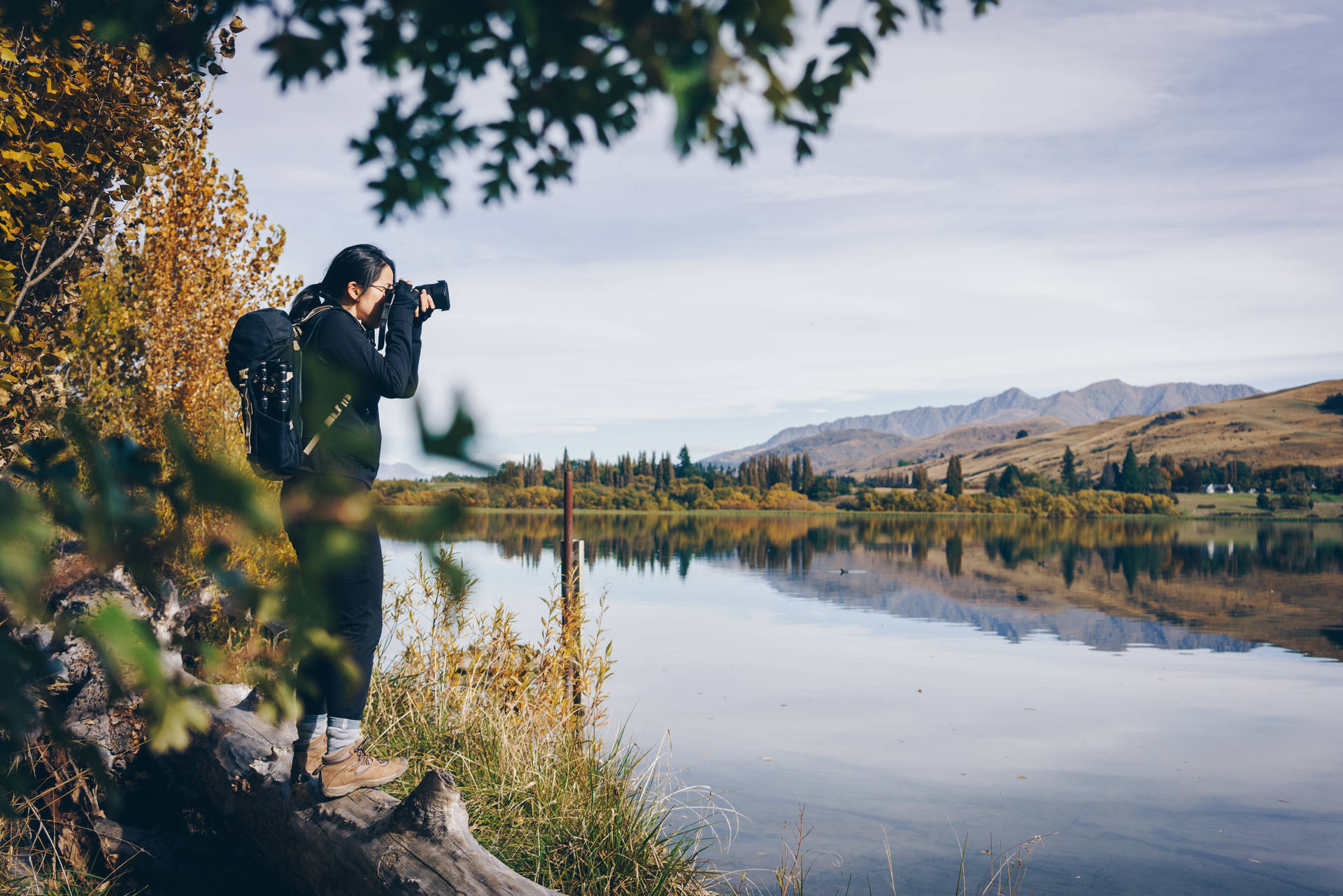 Woman holding a black camera taking a lake photo wallpaper.