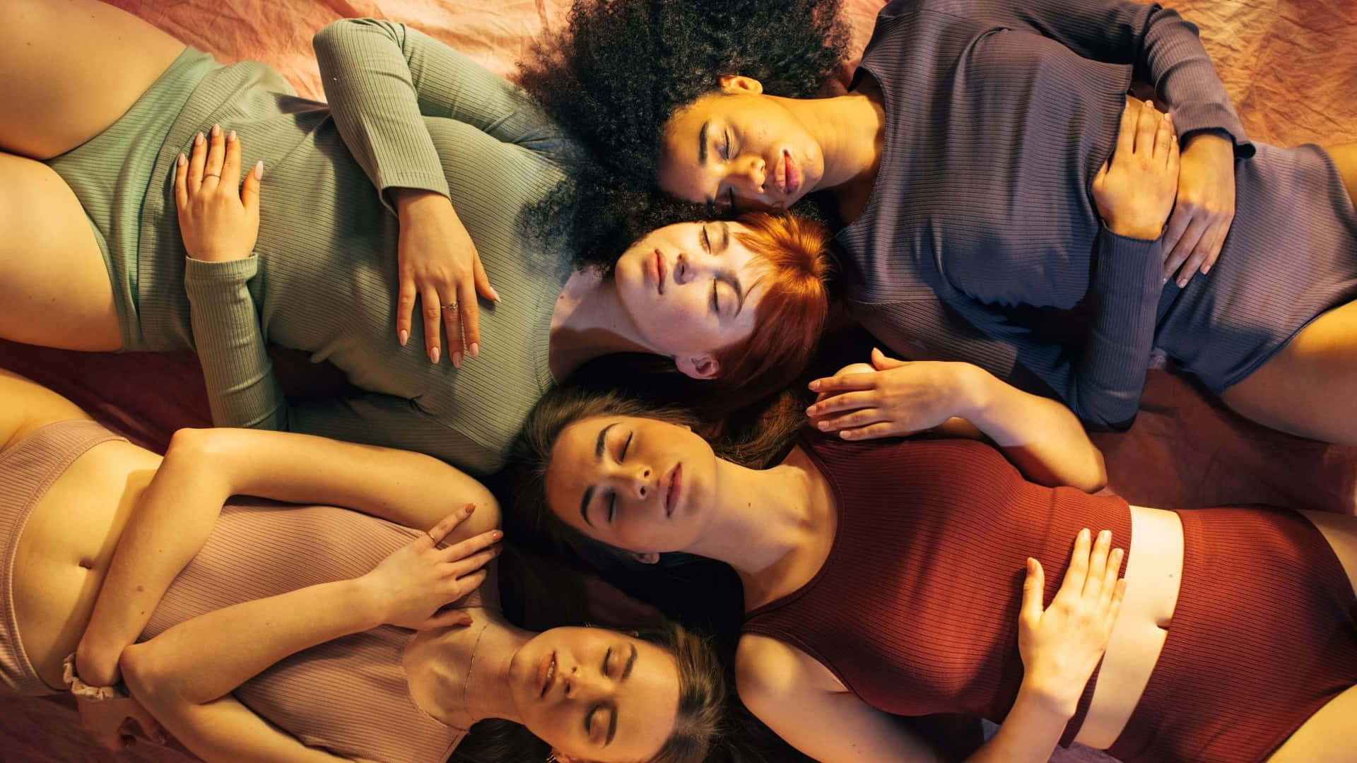 Four Women Laying On A Bed With Their Hands On Their Chests