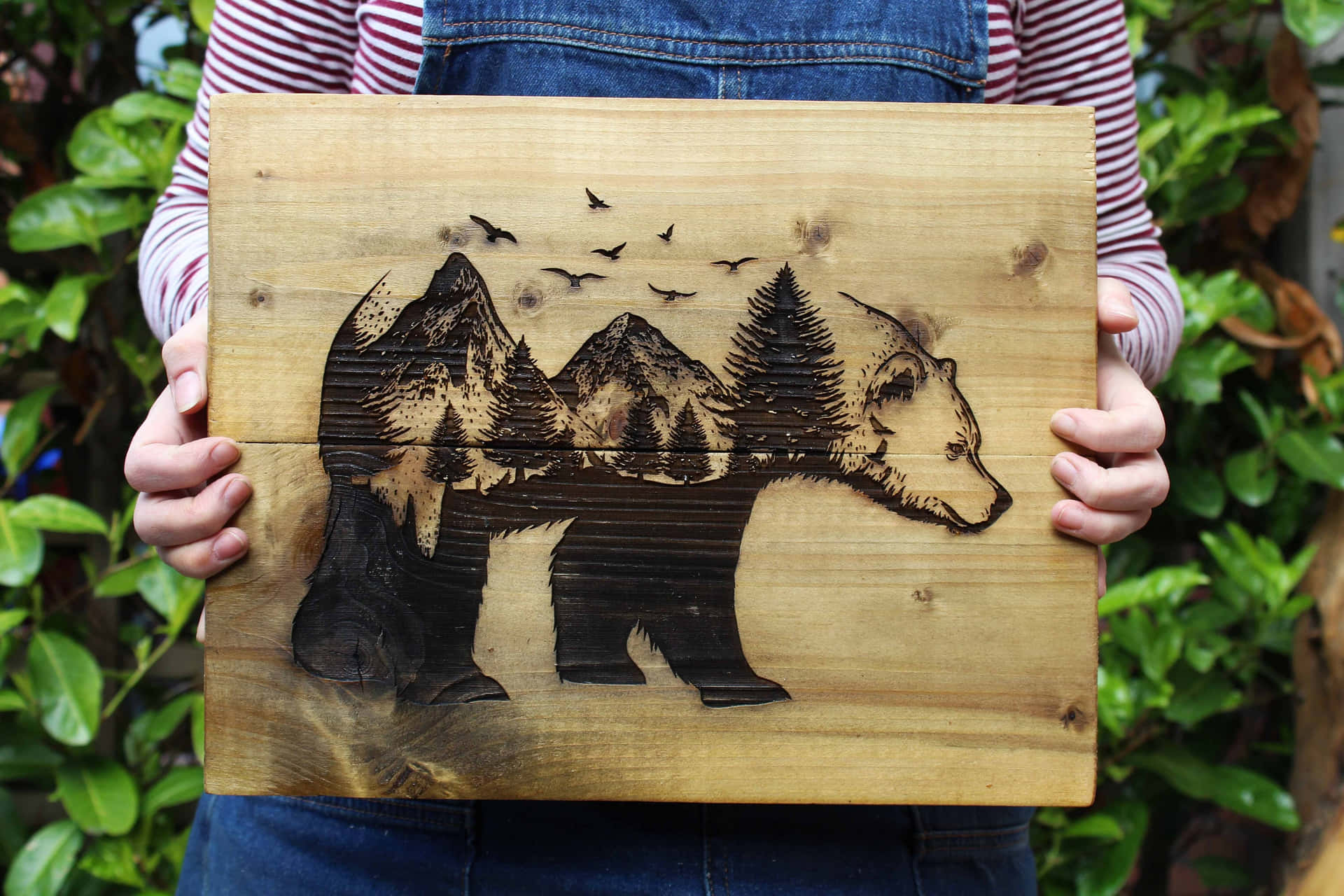 A Woman Holding Up A Wooden Board With A Bear And Trees