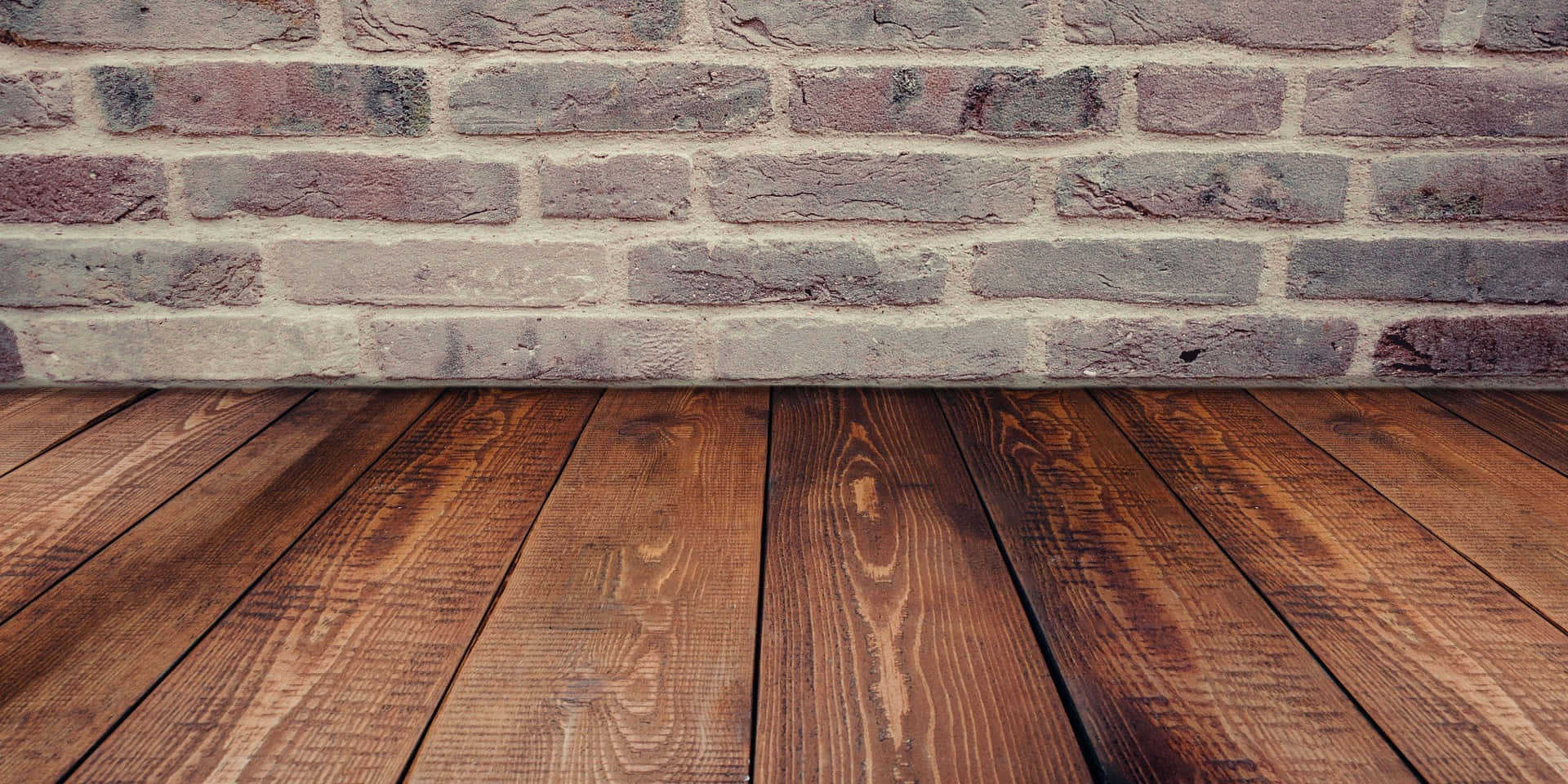 A Wooden Floor With A Brick Wall Behind It