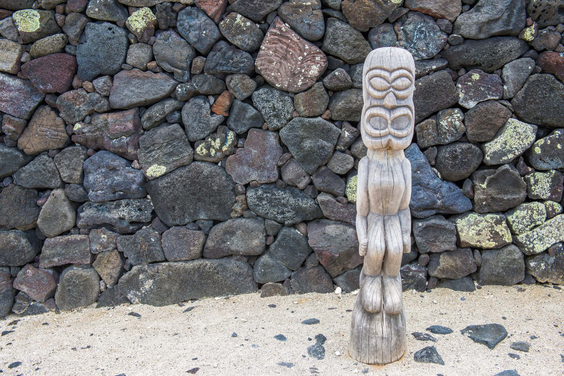 Wooden Tiki Statue Against Stone Wall.jpg Wallpaper
